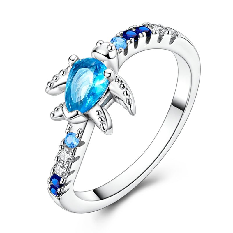 Cette bague en argent 925 met à l’honneur une adorable tortue de mer, sertie d’un cristal bleu en forme de goutte qui évoque immédiatement la transparence des lagons tropicaux. Les petits oxydes de zirconium dégradés du bleu nuit au bleu clair et au blanc se prolongent sur l’anneau, comme une traînée d’écume, pour un bijou lumineux qui rappelle la liberté de l’océan à chaque mouvement de la main.