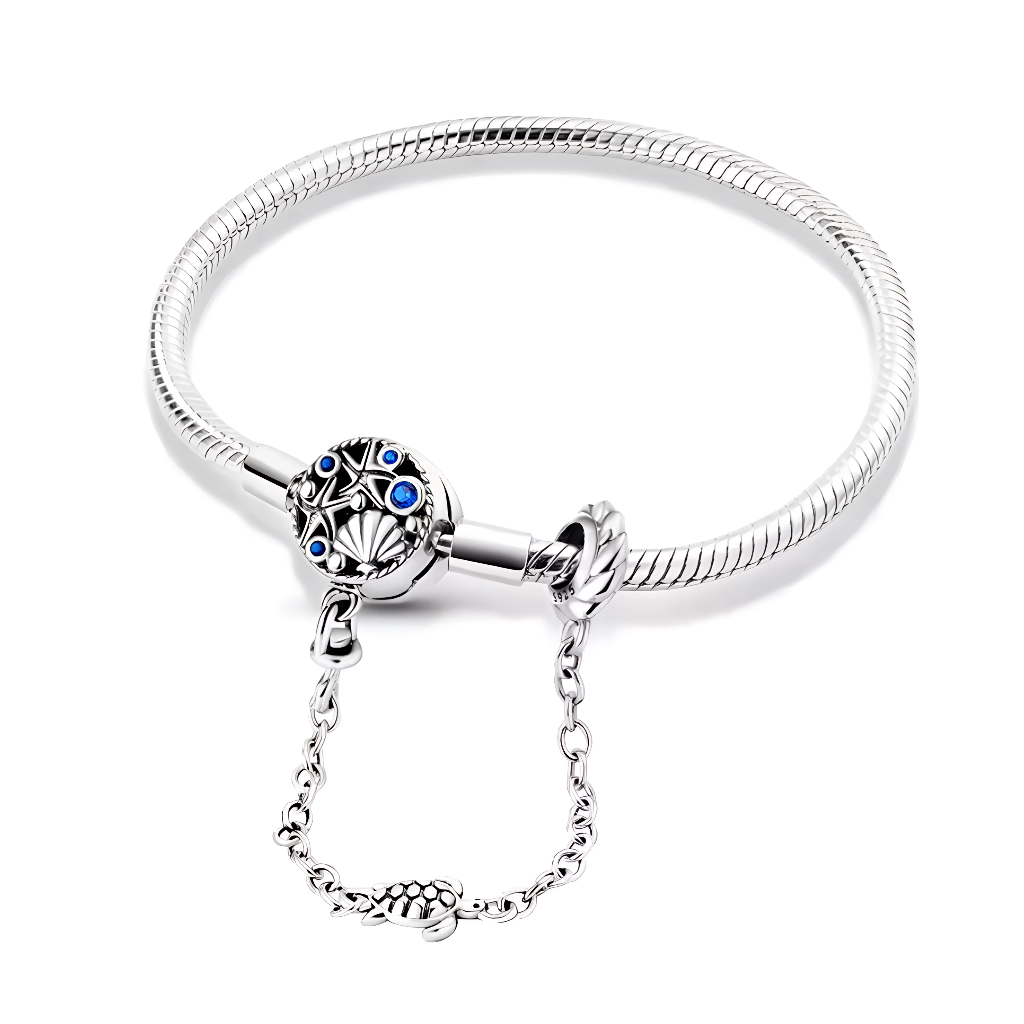Ce bracelet en argent 925 présente un fermoir disque finement travaillé, orné d’une étoile marine, d’un coquillage et de petites pierres bleues rappelant les reflets de l’océan.
La chaîne de sécurité terminée par une petite tortue ajoute une touche ludique tout en protégeant vos charms en cas d’ouverture du fermoir.