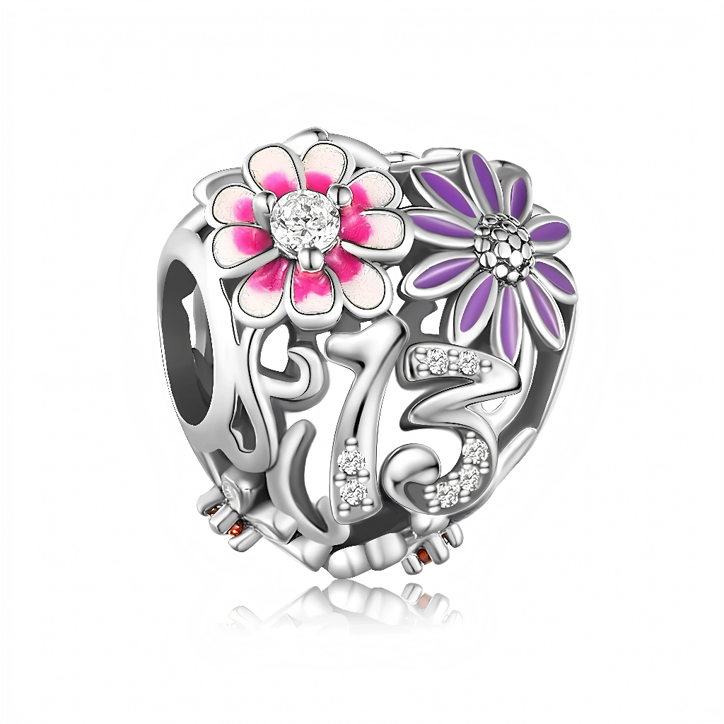 Ce charm ajouré met en avant le chiffre 13, illuminé de petits oxydes de zirconium qui rappellent l’éclat d’un anniversaire inoubliable. Deux fleurs émaillées, l’une rose et l’autre violette, apportent une touche de couleur joyeuse et féminine, évoquant la croissance, la douceur et la découverte d’un nouveau chapitre de vie. L’ensemble crée un bijou à la fois tendre et stylé, parfait comme cadeau souvenir pour une jeune adolescente ou pour personnaliser un bracelet anniversaire.