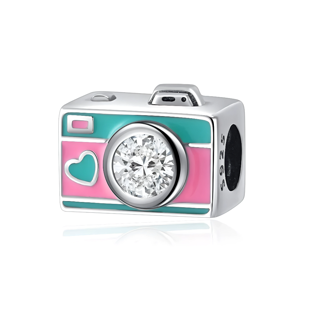 Ce charm en argent prend la forme d’un appareil photo vintage, décoré d’émail rose et vert menthe avec un petit cœur sur la façade. L’objectif est remplacé par un grand cristal clair facetté qui capte la lumière, parfait pour symboliser la passion de la photographie et les souvenirs précieux.