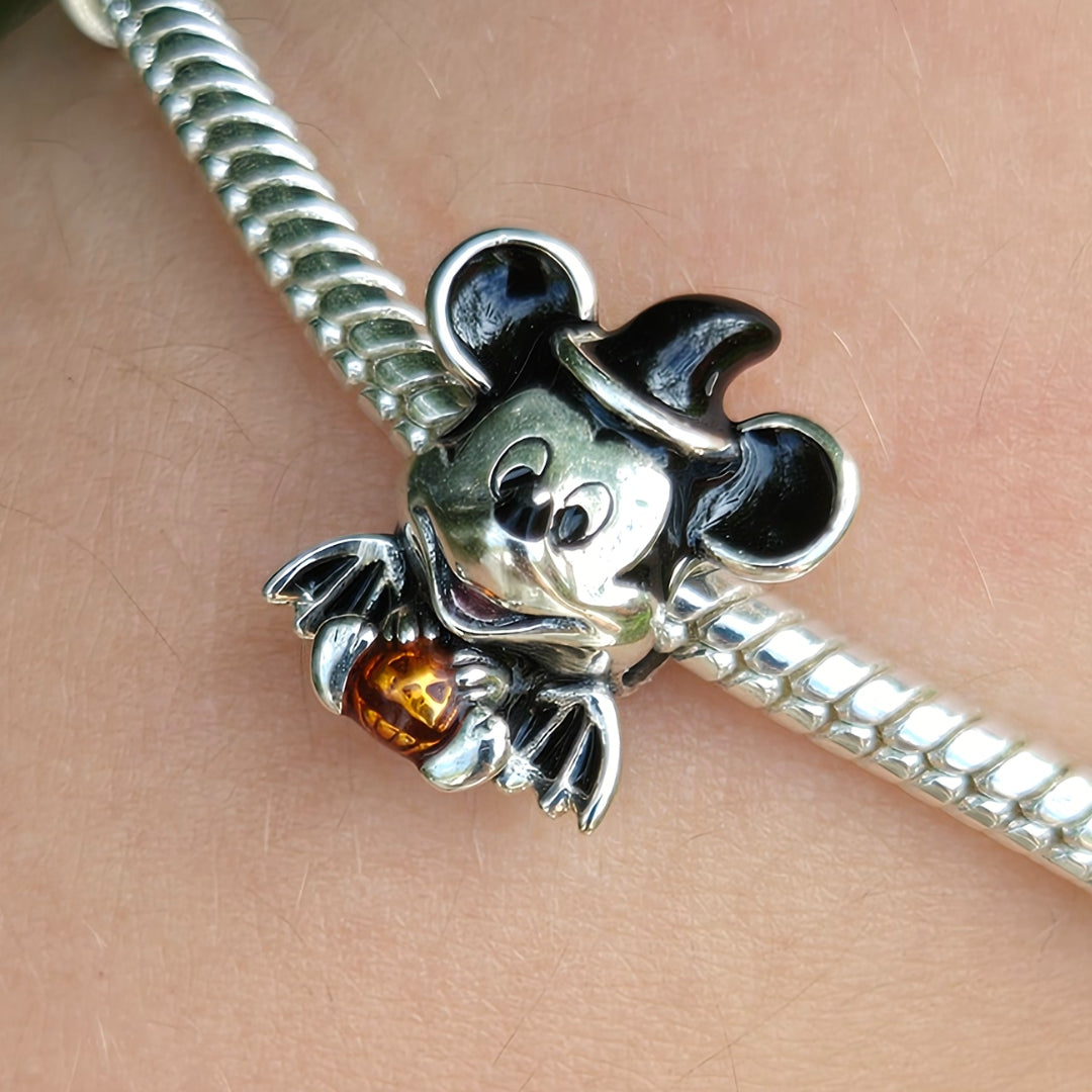 Plongez dans l’esprit d’Halloween avec ce charm unique représentant bébé Mickey assis, portant un chapeau de sorcier noir et de petites ailes noires. Devant lui, une citrouille orange éclatante ajoute une touche de couleur festive à ce bijou réalisé en Argent 925 (S925) avec une finition noir et argent. Parfait pour apporter une ambiance mystérieuse et adorable à votre collection pendant la saison des sorcières.