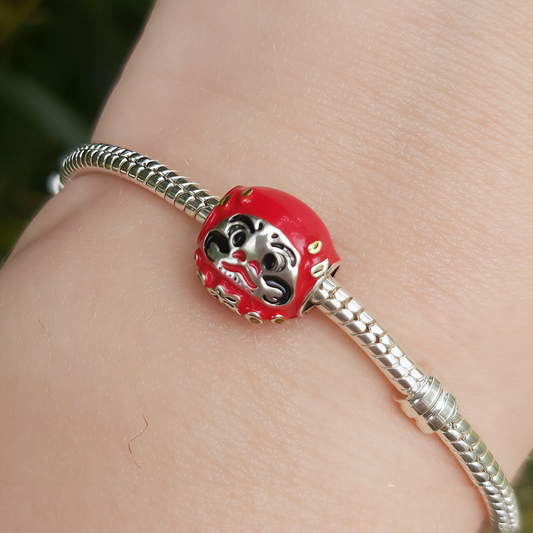 Célébrez la prospérité et la détermination avec ce charm représentant un Daruma rouge, symbole japonais de chance et de persévérance. Fabriqué en argent sterling S925, ce charm est orné de détails raffinés qui capturent l'essence du célèbre porte-bonheur japonais. Le Daruma est un symbole de succès et de bonne fortune, parfait pour accompagner vos objectifs et vos rêves. Compatible avec les bracelets Pandora, il apportera une touche culturelle et porteuse de sens à votre collection.