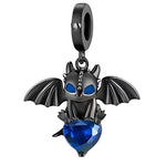 Ce charm pendant en métal noirci représente un petit dragon au style cartoon, ailes déployées et grands yeux bleus intenses. Assis, il enlace un cœur en cristal bleu facetté qui capte la lumière à chaque mouvement, apportant une touche à la fois mystérieuse et tendre au bracelet.

Caractéristiques :
Matière : Alliage métal noirci avec cristal synthétique bleu.
Design : Petit dragon ailé tenant un cœur facetté, suspendu à une bélière lisse.
Coloris : Noir graphite, bleu saphir lumineux.
Compatibilité : Convi