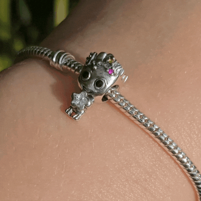 Ajoutez une touche festive et adorable à votre collection avec ce charm Groot en mode Noël. Fabriqué en métal argenté avec des accents de couleur en émail rouge et vert, ce charm représente Groot, le célèbre personnage des Gardiens de la Galaxie, enveloppé dans une guirlande de Noël scintillante, prêt à célébrer les fêtes. Les détails minutieux capturent son expression malicieuse et son côté espiègle, parfait pour les fans de Marvel et de la magie de Noël. Compatible avec les bracelets Pandora, ce charm uni