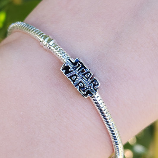 Affichez votre passion pour l'univers galactique avec ce charm représentant le logo emblématique de Star Wars. Conçu en argent sterling S925, ce charm allie élégance et qualité, capturant parfaitement le logo iconique de la saga.