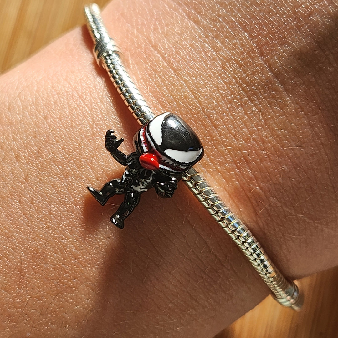 Ajoutez une touche audacieuse et mystérieuse à votre collection avec ce charm Venom Version 2. Fabriqué en métal noirci et rehaussé de détails argentés, ce charm capture l'intensité du personnage légendaire avec une finition détaillée et une expression féroce. Le design met en avant son visage emblématique, avec une langue sinueuse et des crocs acérés, symbolisant la dualité entre pouvoir et chaos. Parfait pour les fans de l'univers des super-héros et des anti-héros, ce charm est compatible avec les bracele
