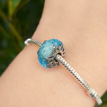 Apportez une touche hivernale à votre collection avec ce charm en verre de Murano Flocon de Neige. Ce bijou raffiné en verre de Murano présente des nuances cristallines et glacées, capturant la magie de l’hiver et l’élégance des flocons de neige. Avec des détails délicats en argent S925 et une compatibilité parfaite avec les bracelets Pandora, ce charm est idéal pour ajouter un éclat saisonnier tout en restant chic et intemporel. Idéal pour les amoureux de l'hiver et ceux qui apprécient la beauté naturelle 