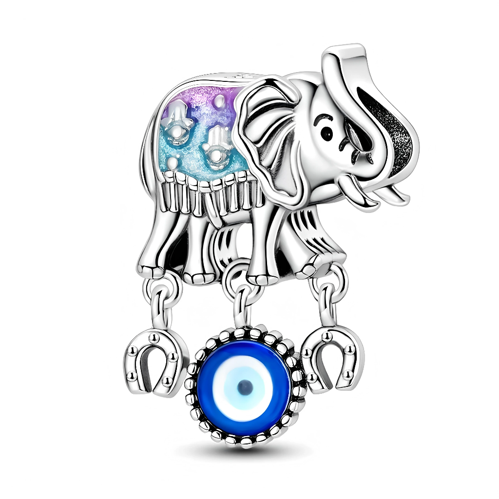 L’éléphant en argent 925 présente un caparaçon émaillé dans des tons bleu et violet, rehaussé de petits motifs et franges gravés qui rappellent les éléphants de fête orientaux. Trois petites chaînes sous le ventre tiennent deux fers à cheval stylisés et un disque central en verre bleu façon Nazar, symbole d’« evil eye » protecteur. L’ensemble combine ainsi plusieurs porte‑bonheur traditionnels : l’éléphant pour la sagesse et la chance, le fer à cheval pour la bonne fortune, et l’œil bleu pour repousser les 
