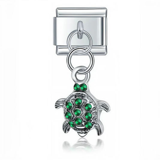 Ce charm italien pendentif représente une tortue délicate ornée de strass verts scintillants, symbole de longévité et de nature. Fabriqué en acier inoxydable de haute qualité avec une finition argentée élégante, il allie robustesse et finesse des détails pour un rendu raffiné et lumineux. Facile à fixer, il s’adapte parfaitement à nos bracelets composés de 17 maillons extensibles et réglables, convenant à toutes les tailles de poignet. Compatible avec tous nos charms italiens, ce bijou étincelant est idéal 