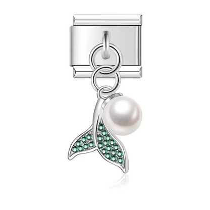 Ce charm pendentif italien en acier inoxydable argenté représente un dauphin formant un cœur délicat, agrémenté d’une perle au centre. Disponible en bleu, rose ou vert, il incarne la tendresse et l’élégance marine. Parfait pour personnaliser votre bracelet, ce pendentif s’adapte à nos bracelets composés de 17 maillons extensibles et réglables, convenant à toutes les tailles de poignet. Compatible avec tous nos charms italiens, il est idéal pour ajouter une touche raffinée et océanique à votre collection.