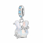 Ce charm pendant en argent 925 représente un petit lapin stylisé entièrement formé d’une pierre synthétique opalescente aux reflets laiteux et irisés, lui donnant un aspect doux et lumineux. Trois petits nœuds en argent viennent s’y poser, tandis que la bélière est soigneusement pavée d’oxydes de zirconium blancs et de cristaux bleu clair pour une touche fraîche et scintillante.