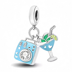 Ce charm réunit un petit appareil photo émaillé bleu ciel avec un cristal clair au centre de l’objectif et un verre à cocktail assorti décoré de cœurs blancs. Les feuilles vertes, les quartiers d’agrume et les pailles qui dépassent du verre créent une ambiance estivale et dépaysante, parfaite pour rappeler les voyages et les moments immortalisés en photo sur un bracelet ou un collier.