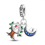 La bélière en argent 925 est décorée de cœurs ajourés et de zircons clairs qui forment un anneau scintillant. Deux pendentifs y sont suspendus : à gauche, un tronc brun émaillé portant un nichoir blanc au cœur rouge entouré de feuilles vertes, à droite un croissant de lune serti de cristaux bleus avec une étoile argentée en relief.