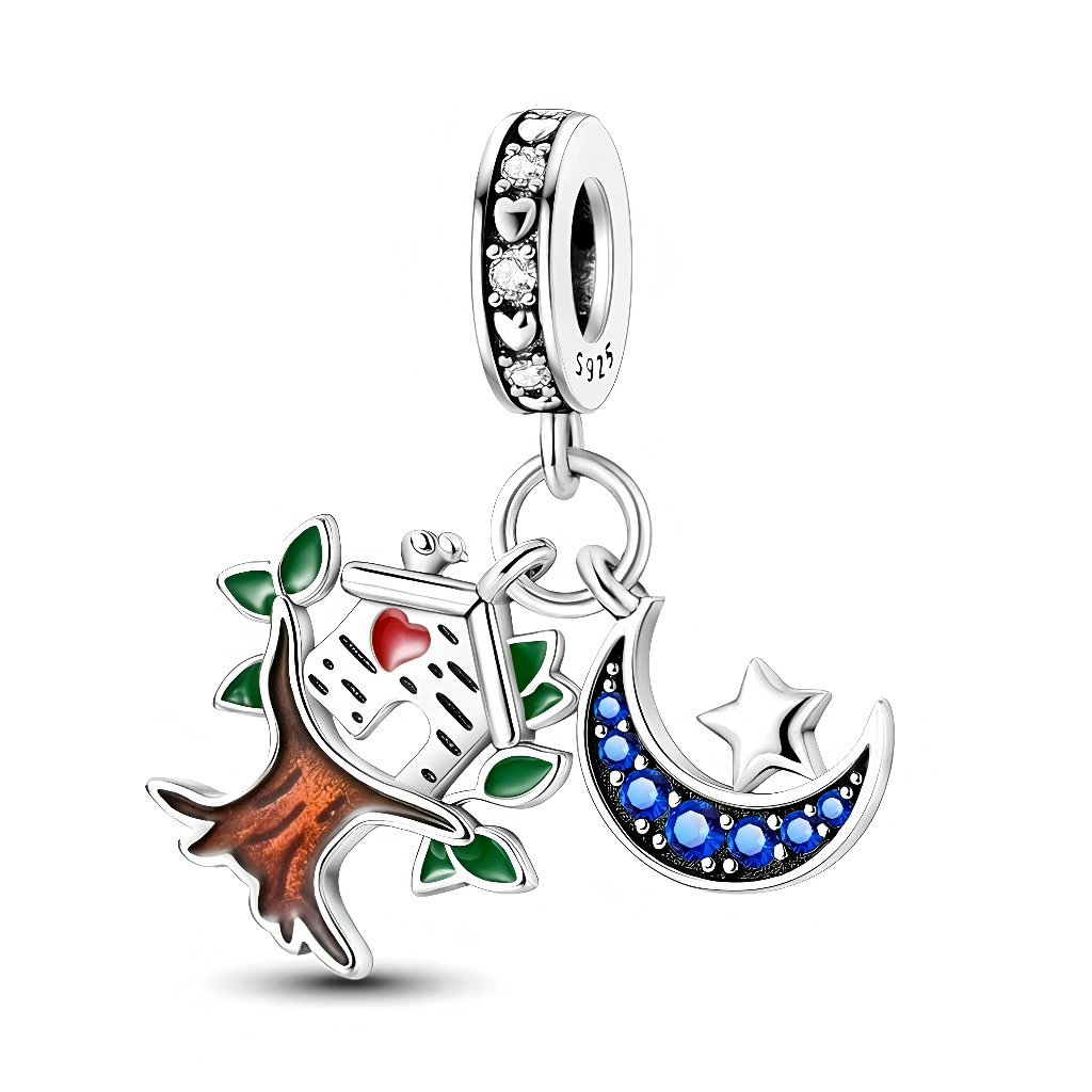 La bélière en argent 925 est décorée de cœurs ajourés et de zircons clairs qui forment un anneau scintillant. Deux pendentifs y sont suspendus : à gauche, un tronc brun émaillé portant un nichoir blanc au cœur rouge entouré de feuilles vertes, à droite un croissant de lune serti de cristaux bleus avec une étoile argentée en relief.