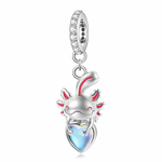 Suspendu à une bélière pavée de petits zircons, l’axolotl en argent arbore un large sourire et des branchies rosées qui ressortent délicatement sur le métal brillant. Entre ses pattes, il tient un grand cœur en pierre opalescente aux reflets bleus, qui change de couleur selon la lumière et évoque un trésor aquatique. L’ensemble crée un bijou ludique et attendrissant, parfait pour symboliser la bienveillance, la singularité et l’amour qui sort de l’ordinaire.
