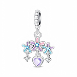 Trois marguerites émaillées dans des tons rose, lavande et bleu turquoise forment une mini guirlande florale, chacune centrée par un petit cristal bleu vif. Sous la fleur centrale, un cœur facetté violet pâle est suspendu comme un petit pendentif, tandis que deux breloques cristallines plus petites encadrent l’ensemble pour un rendu très lumineux et mobile. La bélière texturée apporte une touche raffinée et permet de porter ce charm aussi bien sur un bracelet que sur un collier.