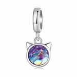 Ce charm pendentif en argent 925 représente une petite tête de chat stylisée, dont le visage est remplacé par un cabochon rond aux reflets holographiques violets, bleus et dorés rappelant des écailles de sirène. La bélière lisse et polie offre un tombé épuré qui met en valeur les couleurs changeantes du cabochon à chaque mouvement.