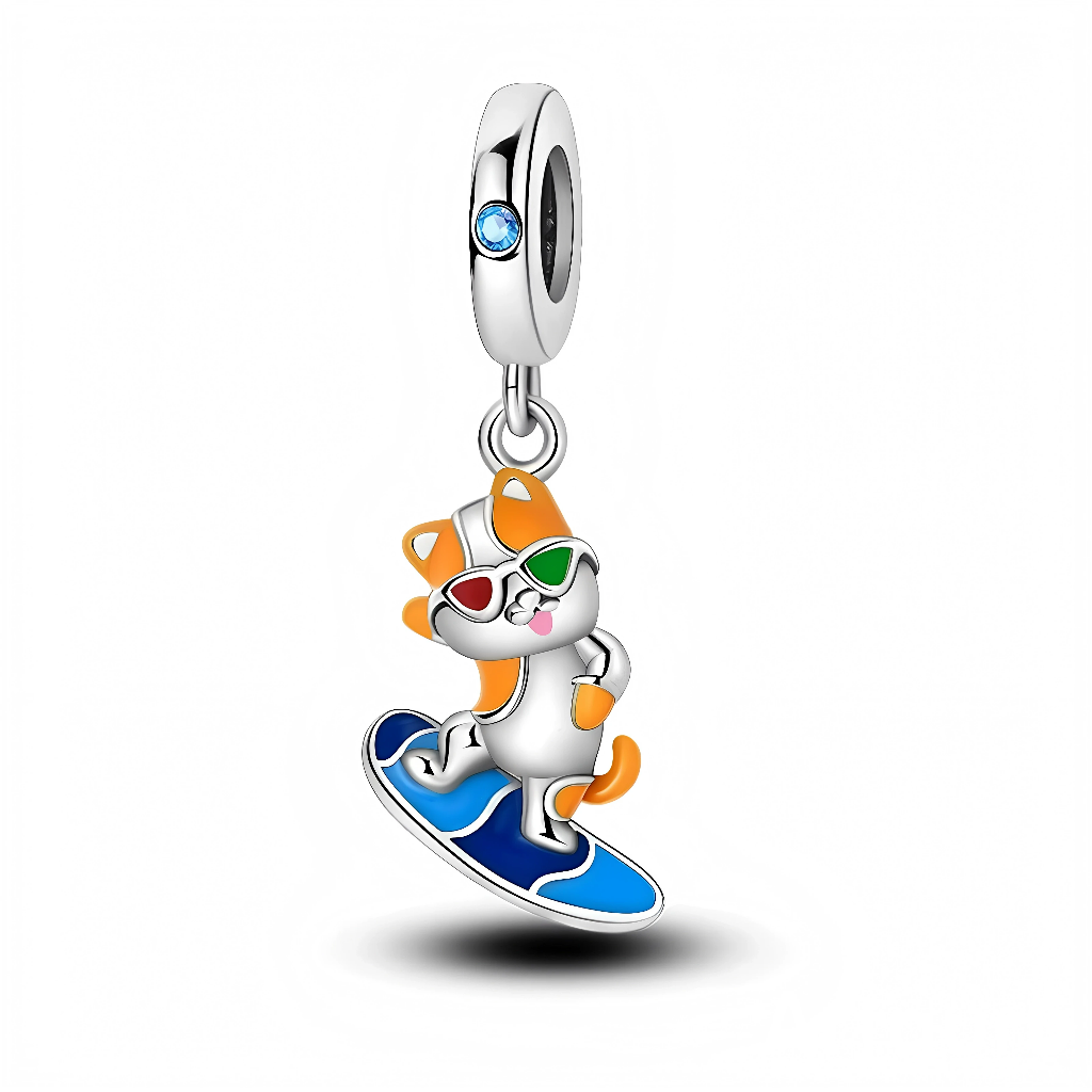 La bélière en argent 925 est rehaussée d’un petit cristal bleu qui rappelle la couleur de l’océan. Le pendentif représente un chat orange et blanc avec des lunettes de soleil multicolores, debout sur une planche de surf émaillée de bleus vifs, dans une pose dynamique.