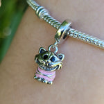 Ajoutez une touche de folie et de mystère à votre collection avec ce charm pendentif du célèbre Chat du Cheshire, issu de l’univers d’Alice au Pays des Merveilles. Assis dans sa posture emblématique, ce personnage malicieux est ici représenté en finition argentée brillante, avec un corps rose rayé fidèle à son design original. Son sourire énigmatique et son regard espiègle font de ce bijou un clin d'œil parfait à l'imaginaire décalé de Lewis Carroll.