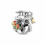 Ce charm en argent 925 représente une chouette savante coiffée d’un chapeau de graduation, tenant un petit bouquet de fleurs colorées dans son aile, symbole de réussite et de célébration. Un mini pendentif rectangulaire jaune façon diplôme est suspendu à son chapeau, apportant une touche de mouvement et d’éclat supplémentaire.