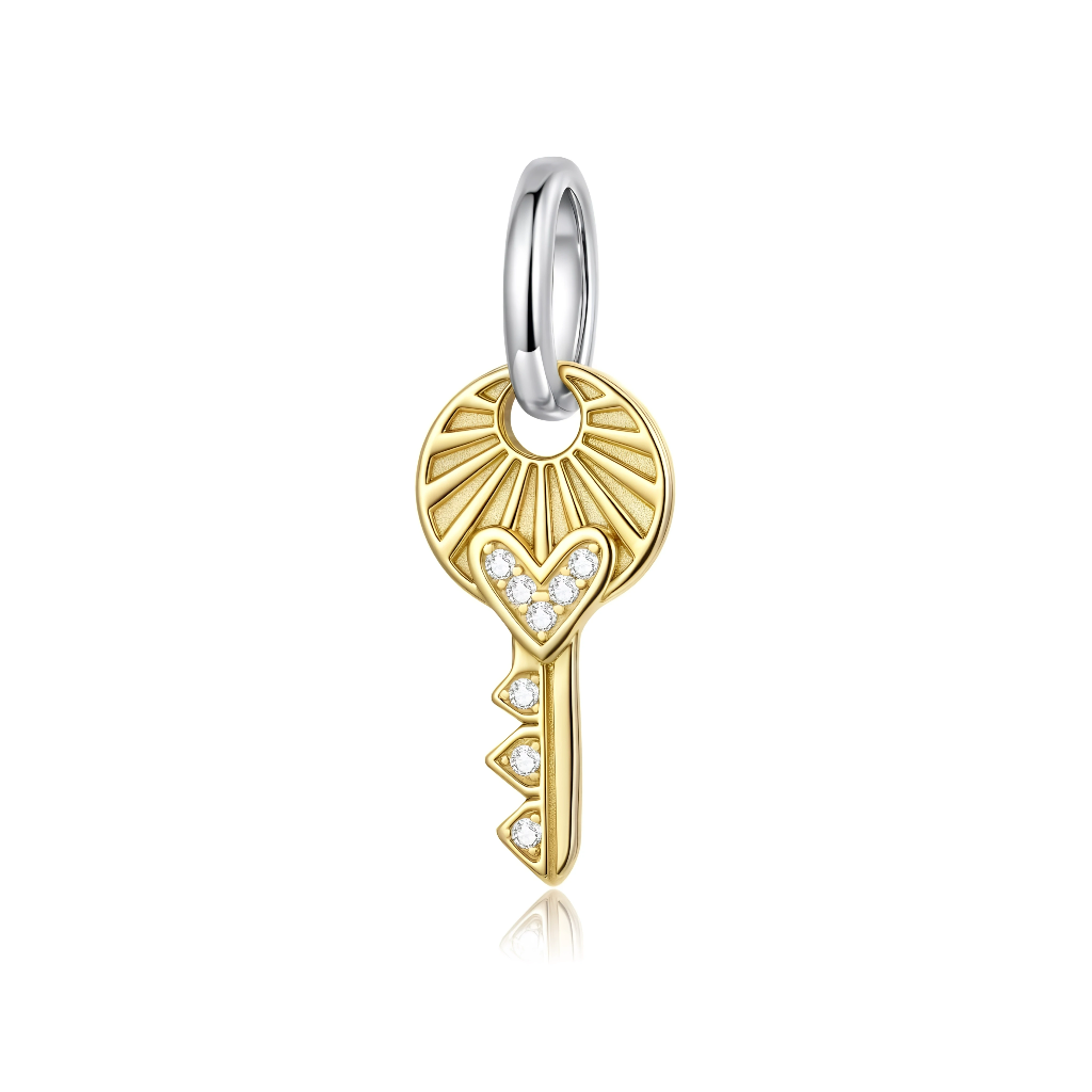 La clé est plaquée or sur une base en argent 925, avec un cercle supérieur décoré de fins rayons façon soleil levant. La partie en forme de cœur ainsi que trois petits détails triangulaires le long de la tige sont incrustés de zircons cubiques transparents pour un éclat délicat.
