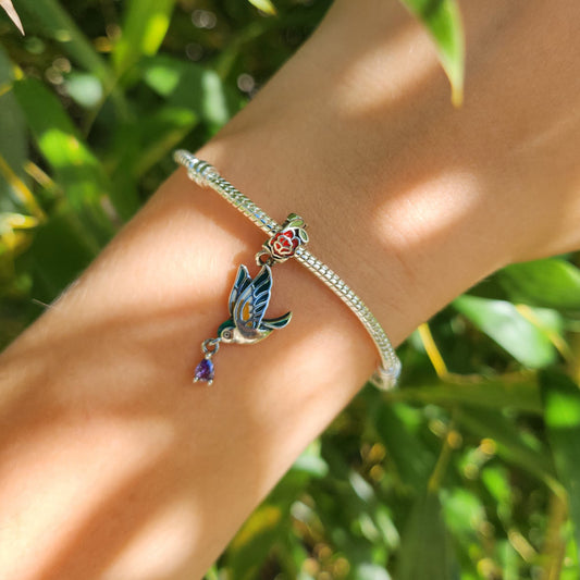 Ajoutez une touche de grâce et de beauté naturelle à votre collection avec ce charm représentant un colibri en vol, orné de délicates pivoines. Fabriqué en argent sterling S925, ce charm allie élégance et finesse, capturant la légèreté et le charme du colibri ainsi que la beauté des pivoines.