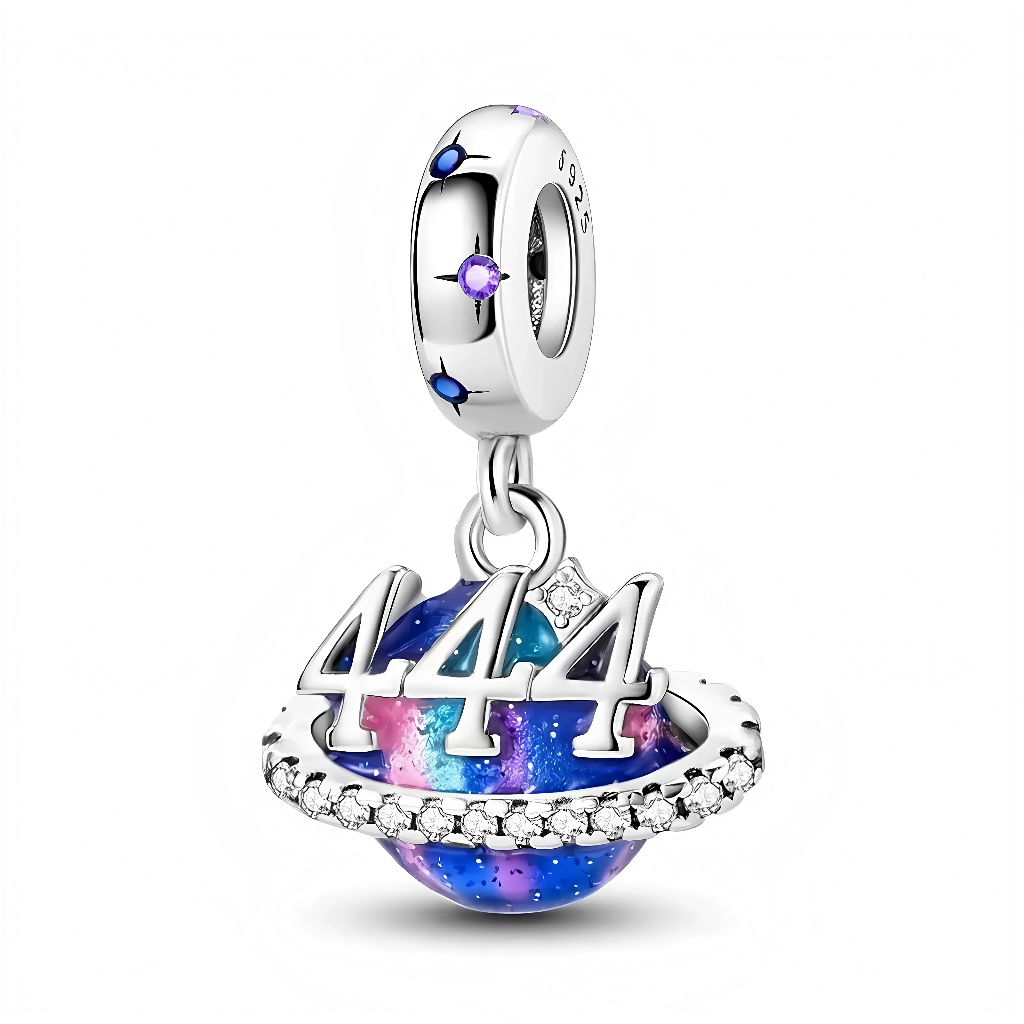 La bélière en argent 925 est décorée de petites étoiles bleu foncé et pierres violettes, rappelant un ciel nocturne. En dessous, une sphère émaillée façon nébuleuse porte un anneau serti de cristaux transparents, sur lequel se détache le chiffre 444 en relief, souvent associé à la protection, à la stabilité et à l’abondance dans les interprétations d’« angel number ».