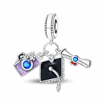 La bélière en argent 925 est texturée de petites billes, à laquelle sont suspendues trois mini-breloques symboliques. On trouve un appareil photo émaillé violet avec une pierre bleue ronde au centre, un chapeau de graduation noir avec pompon détaillé et un diplôme roulé décoré d’un sceau rouge et d’un cristal bleu.