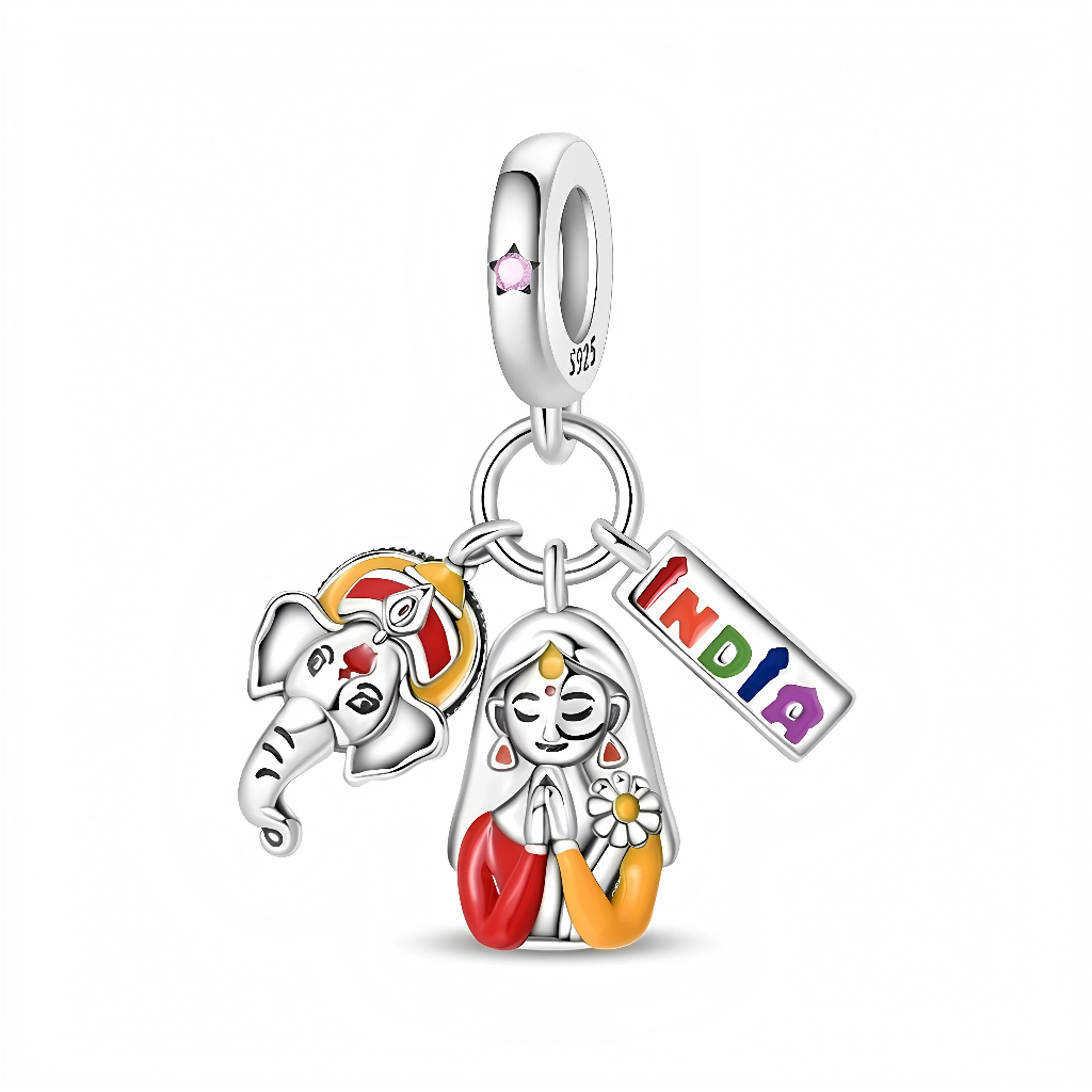 Ce charm pendentif en argent rend hommage à l’Inde avec trois breloques colorées : un visage de divinité éléphantine stylisée, une femme en posture de namasté aux vêtements rouges et safran, et un petit rectangle “India” aux lettres arc-en-ciel. La bélière lisse sertie d’un cristal rose ajoute une touche délicate, idéale pour symboliser un voyage, un attachement culturel ou l’amour de la spiritualité indienne.