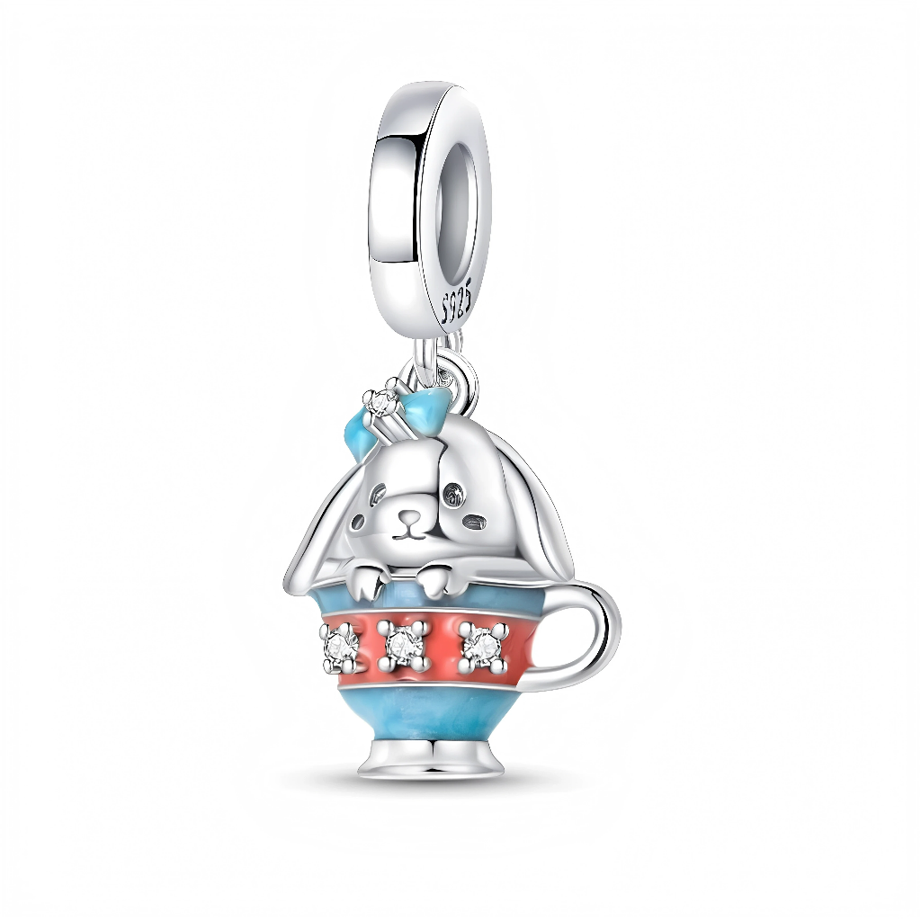 Le lapin en argent 925 dépasse d’une tasse bicolore turquoise et corail, décorée d’une rangée de petits cristaux clairs qui imitent des fleurs autour de la tasse. Sur la tête du lapin, un nœud bleu émaillé et une fleur de zircon ajoutent une touche brillante et féminine, tandis que la bélière lisse porte le poinçon S925. L’ensemble évoque un moment de tea‑time féerique, rappelant les univers de contes et d’Alice au pays des merveilles.