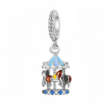 Ce charm pendentif en argent représente un petit carrousel en trois dimensions, avec son toit émaillé de bleu ciel et ses chevaux de bois bruns et gris fixés sur des barres torsadées. La base est sertie d’une alternance de cristaux bleus et transparents, tandis que la bélière décorée de petites billes rappelle l’esprit festif des fêtes foraines et des souvenirs d’enfance.