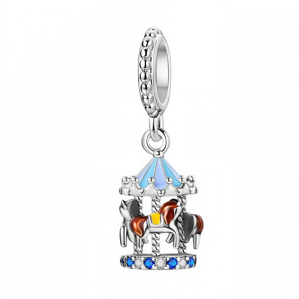 Ce charm pendentif en argent représente un petit carrousel en trois dimensions, avec son toit émaillé de bleu ciel et ses chevaux de bois bruns et gris fixés sur des barres torsadées. La base est sertie d’une alternance de cristaux bleus et transparents, tandis que la bélière décorée de petites billes rappelle l’esprit festif des fêtes foraines et des souvenirs d’enfance.