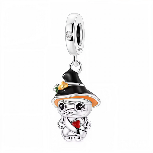 Craquez pour l’originalité de ce charm Halloween qui marie la douceur à la fantaisie ! Il met en scène une petite momie enveloppée de bandelettes argentées, coiffée d’un grand chapeau de sorcière noir décoré de citrouille, et tenant un cœur rouge éclatant. Réalisé en argent 925 avec des touches d’émaux noirs, oranges, rouges et verts, ce bijou se distingue par son design attendrissant et festif. Parfait pour apporter une note tendre et espiègle à vos bracelets à charms au moment d’Halloween.