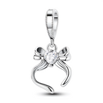 Ce charm pendentif en argent se compose d’un élégant nœud ruban dont les extrémités ondulées encadrent un cristal clair en forme de cœur, parfaitement mis en avant au centre. Sa ligne fine et féminine en fait un bijou discret et raffiné, idéal pour symboliser un cadeau, un lien affectif ou une promesse.