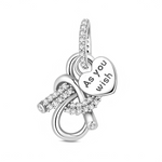 Le design met en scène un grand nœud ouvert en argent dont les courbes se croisent comme un symbole d’infini, entièrement pavé de zircons scintillants pour un rendu très lumineux. Au centre du nœud se balance un cœur lisse portant l’inscription « As you wish », message romantique qui évoque la dévotion, l’écoute et le désir de combler l’être aimé. La bélière, elle aussi sertie de pierres, prolonge l’effet bijou de luxe et permet de porter ce pendentif aussi bien sur un bracelet que sur un collier.