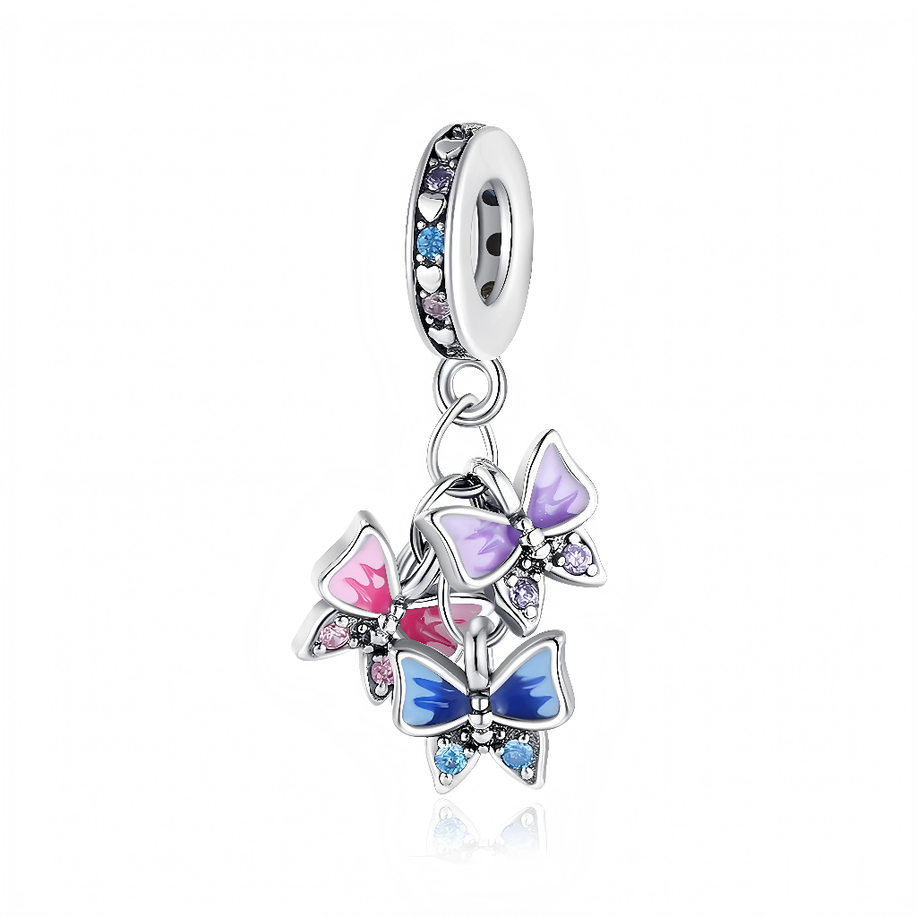 La bélière fine en argent 925 est sertie d’une alternance de zircons violets, roses et bleus, séparés par de petits cœurs argentés gravés dans la monture. En dessous, trois papillons émaillés dans des dégradés de rose, mauve et bleu sont suspendus à de petits anneaux, chacun orné de pierres assorties sur les ailes pour un effet très lumineux et mobile. L’ensemble évoque un essaim de papillons en plein vol, symbole de liberté et de transformation.
