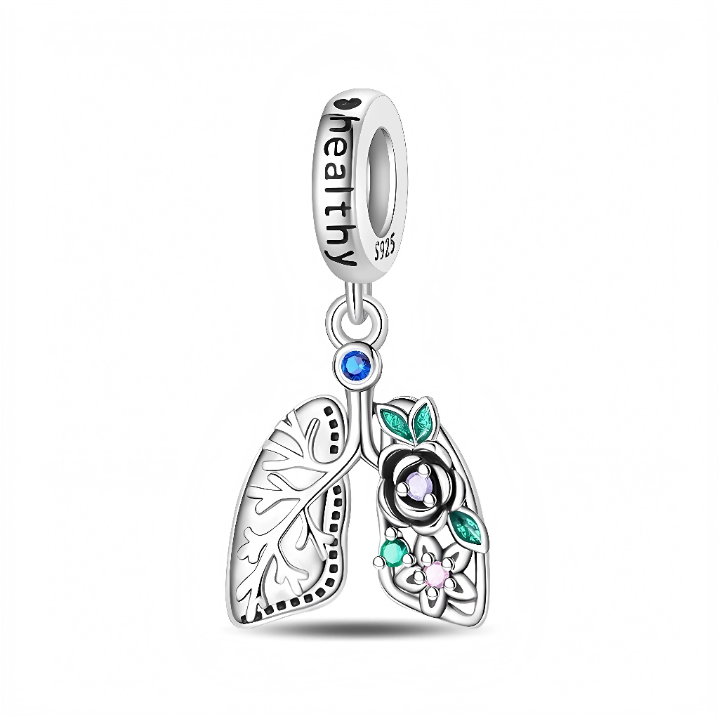 Ce charm pendentif en argent représente une paire de poumons stylisés, dont un côté est finement gravé des ramifications respiratoires tandis que l’autre est décoré de fleurs et de feuilles vertes serties de petits cristaux colorés. Un cristal bleu au sommet relie les poumons à une bélière gravée du mot “healthy”, en faisant un bijou idéal pour symboliser la santé, la respiration, la médecine respiratoire ou un message de guérison.