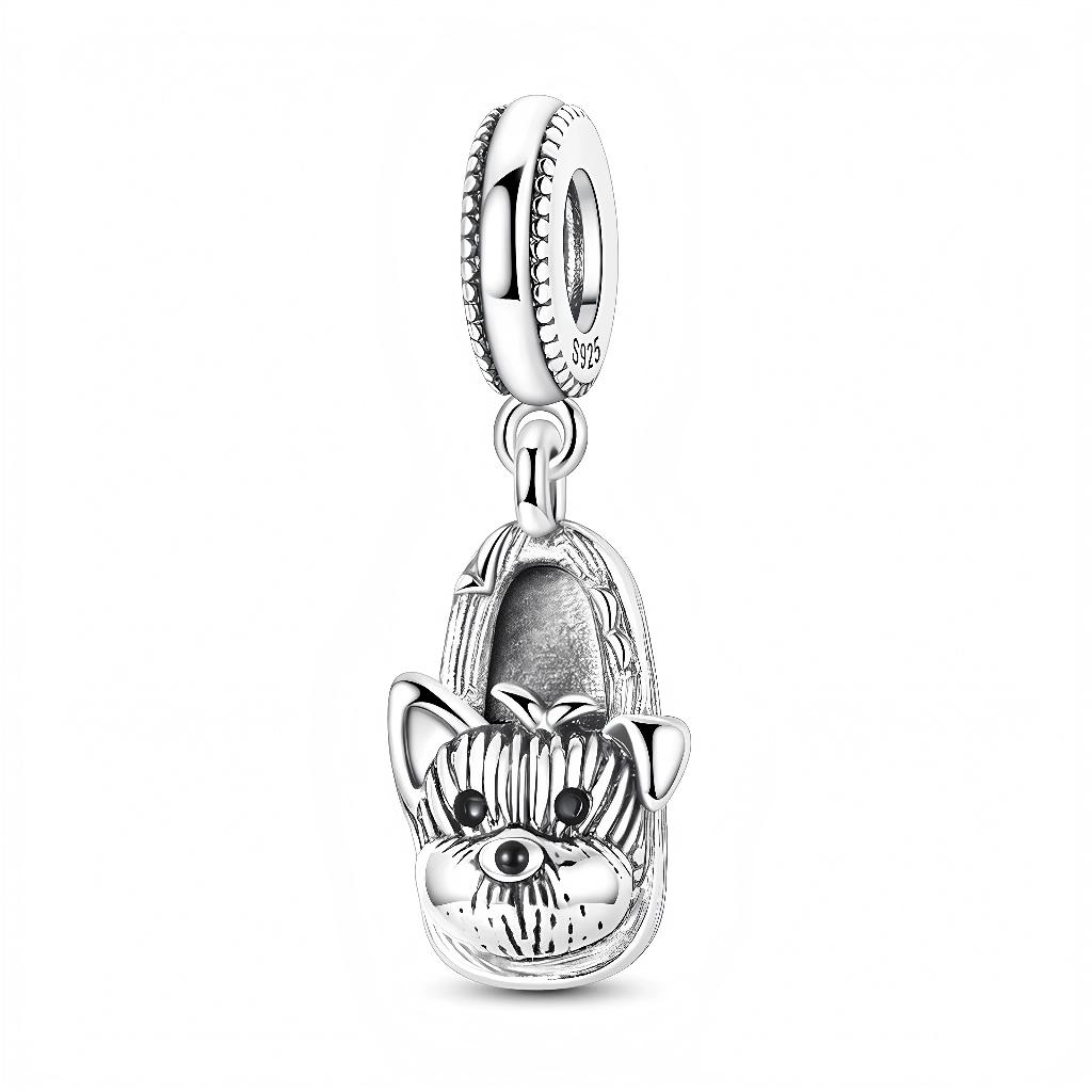 La bélière ronde en argent 925 est ponctuée d’un motif de micro-billes tout autour et reliée au pendentif par un double anneau mobile. Le pendentif figure un chausson détaillé, dont l’avant est sculpté en museau de yorkie avec oreilles dressées, truffe et yeux sombres accentués par de l’oxydation pour faire ressortir le pelage.