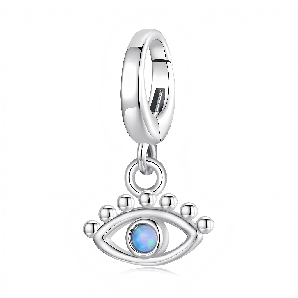 La bélière lisse en argent 925 est sobre et contemporaine, laissant toute l’attention au petit pendentif œil suspendu. L’œil est formé d’un contour ovale argenté agrémenté de petites billes en relief façon cils, avec au centre une pierre type opale synthétique bleu irisé qui rappelle les talismans méditerranéens de protection.