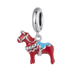 Ce charm pendentif reproduit fidèlement le célèbre dalahäst suédois, un cheval rouge en émail brillant typique de l’artisanat folklorique de Dalarna, symbole national de la Suède. Sa selle bleue ornée de motifs traditionnels kurbits et bordée de pierres claires ajoute une touche d’élégance authentique et festive à cette figurine sculpturale. Le harnais blanc sculpté met en valeur les courbes robustes du cheval, évoquant force, chance et héritage culturel nordique.