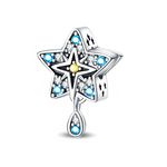 Ce charm représente une grande étoile ajourée en métal argenté, entièrement pavée de petits cristaux blancs et bleus qui lui donnent un éclat nocturne. Au centre, une étoile plus petite soulignée d’un détail doré et une goutte pendante sertie de cristaux apportent du mouvement et un effet talisman lumineux.