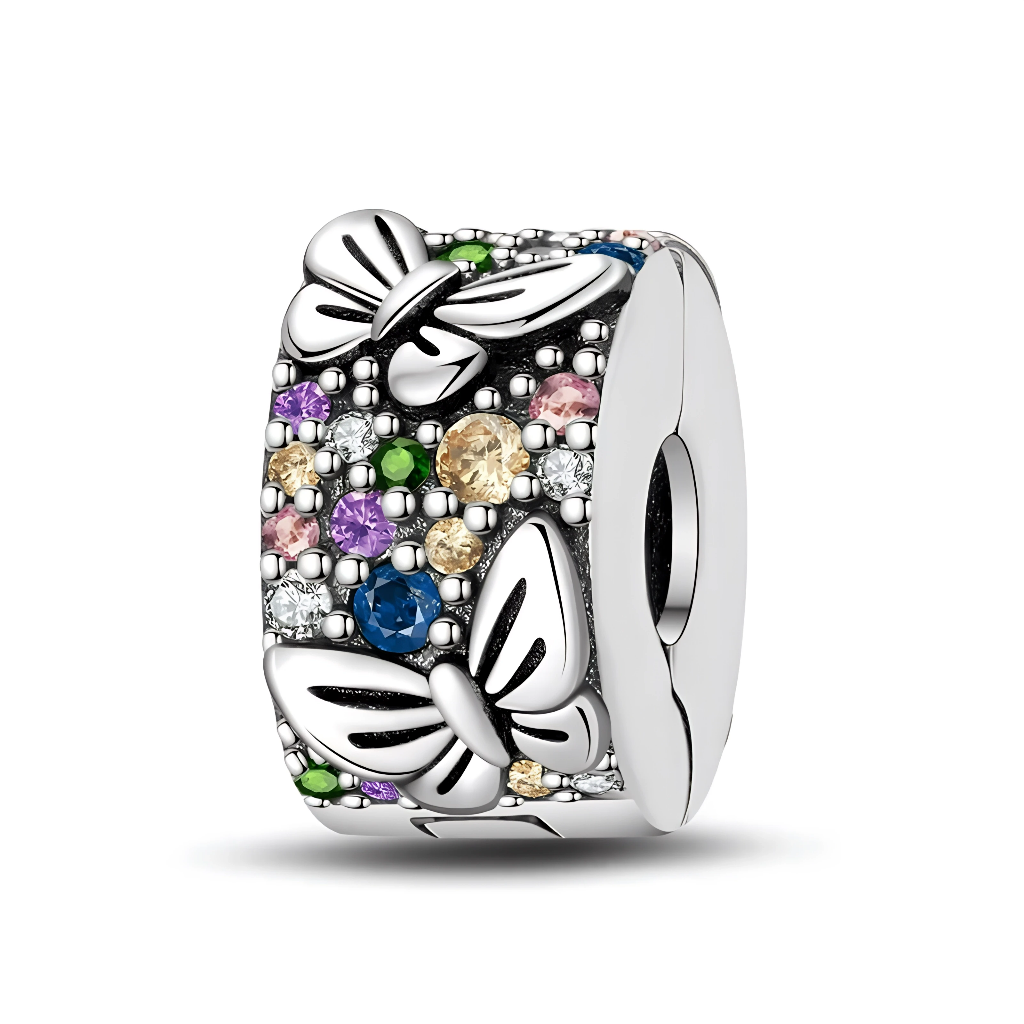 La surface en argent est entièrement pavée de petits cristaux multicolores (bleu, vert, rose, champagne, transparent), créant un effet mosaïque étincelant. Trois grands papillons en relief se détachent sur ce fond scintillant, comme s’ils volaient au-dessus d’un jardin de pierres précieuses. Conçu comme un clip, il se ferme directement sur le bracelet pour structurer la composition et empêcher les autres charms de glisser.