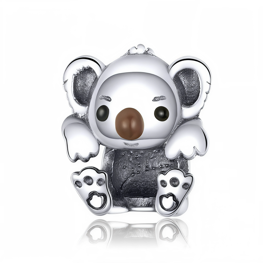 Ce charm représente un petit koala assis, les pattes avant levées comme s’il jouait ou faisait un câlin, avec une expression légèrement malicieuse sur le visage. Son museau brun proéminent et ses grandes oreilles texturées contrastent avec le corps gris foncé, donnant beaucoup de relief au personnage.