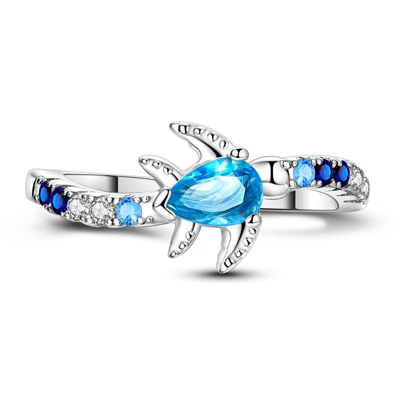 Cette bague en argent 925 met à l’honneur une adorable tortue de mer, sertie d’un cristal bleu en forme de goutte qui évoque immédiatement la transparence des lagons tropicaux. Les petits oxydes de zirconium dégradés du bleu nuit au bleu clair et au blanc se prolongent sur l’anneau, comme une traînée d’écume, pour un bijou lumineux qui rappelle la liberté de l’océan à chaque mouvement de la main.