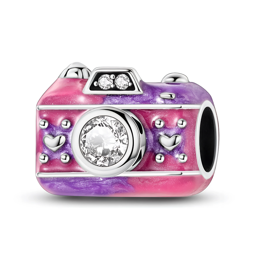 Ce charm en argent 925 prend la forme d’un appareil photo vintage, habillé d’un émail dégradé rose et violet parsemé de petits cœurs en relief. Une grande pierre claire ronde occupe la place de l’objectif, tandis que deux petits cristaux brillent sur le « flash » pour un effet ultra scintillant.