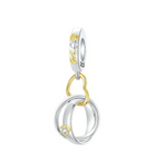 Ce charm pendentif en argent 925 met en scène deux anneaux de mariage entrelacés, l’un rehaussé d’un petit zircon clair serti dans un chaton doré, symbolisant l’union et l’engagement. Les alliances sont suspendues à un anneau en forme de cœur, lui‑même accroché à une bélière lisse décorée d’un motif doré fluide pour une touche raffinée.